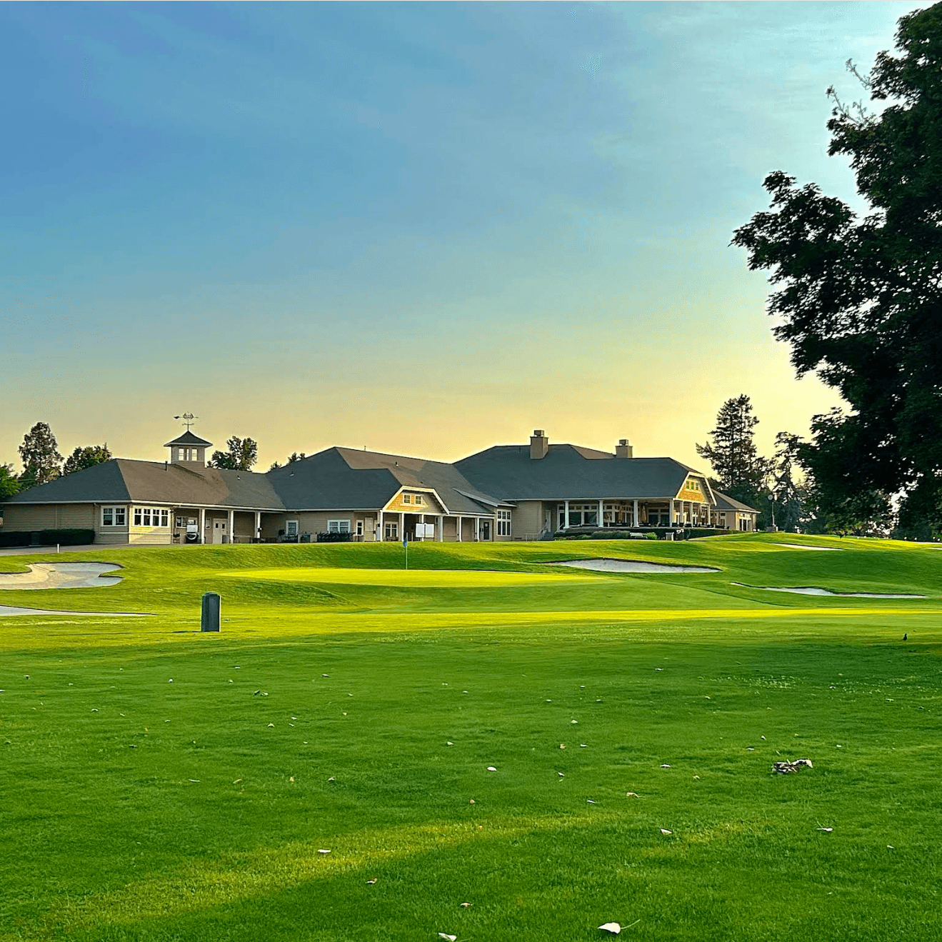 A golf clubhouse with a manicured lawn and a clear sky at sunset.