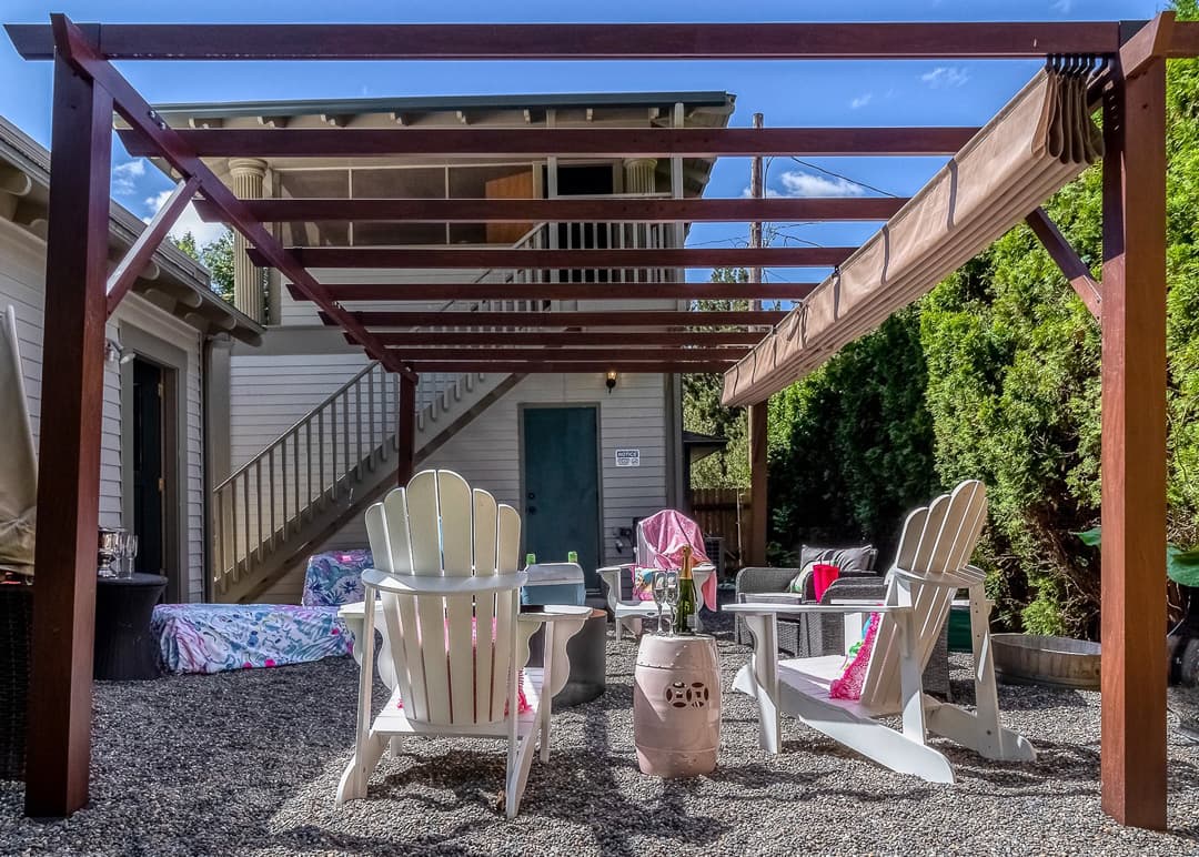 Outdoor seating area with white chairs and a wooden pergola in a gravel space.