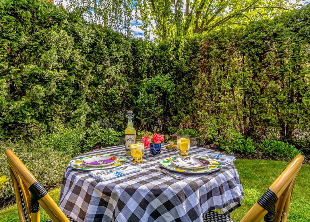 A table set for a garden meal with colorful plates, drinks, and greenery in the background.