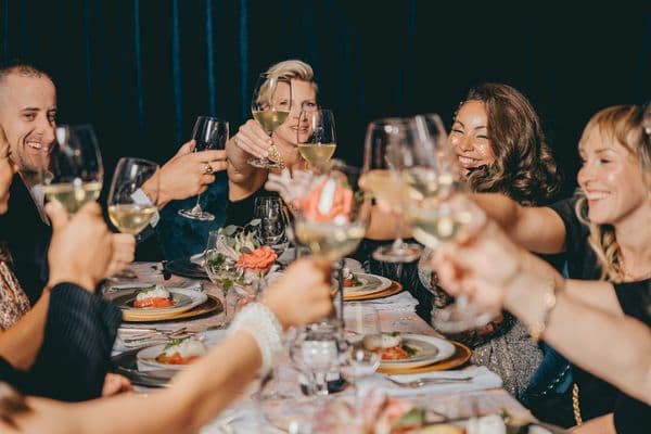 A group of people toasting with glasses of white wine at a festive dinner table.