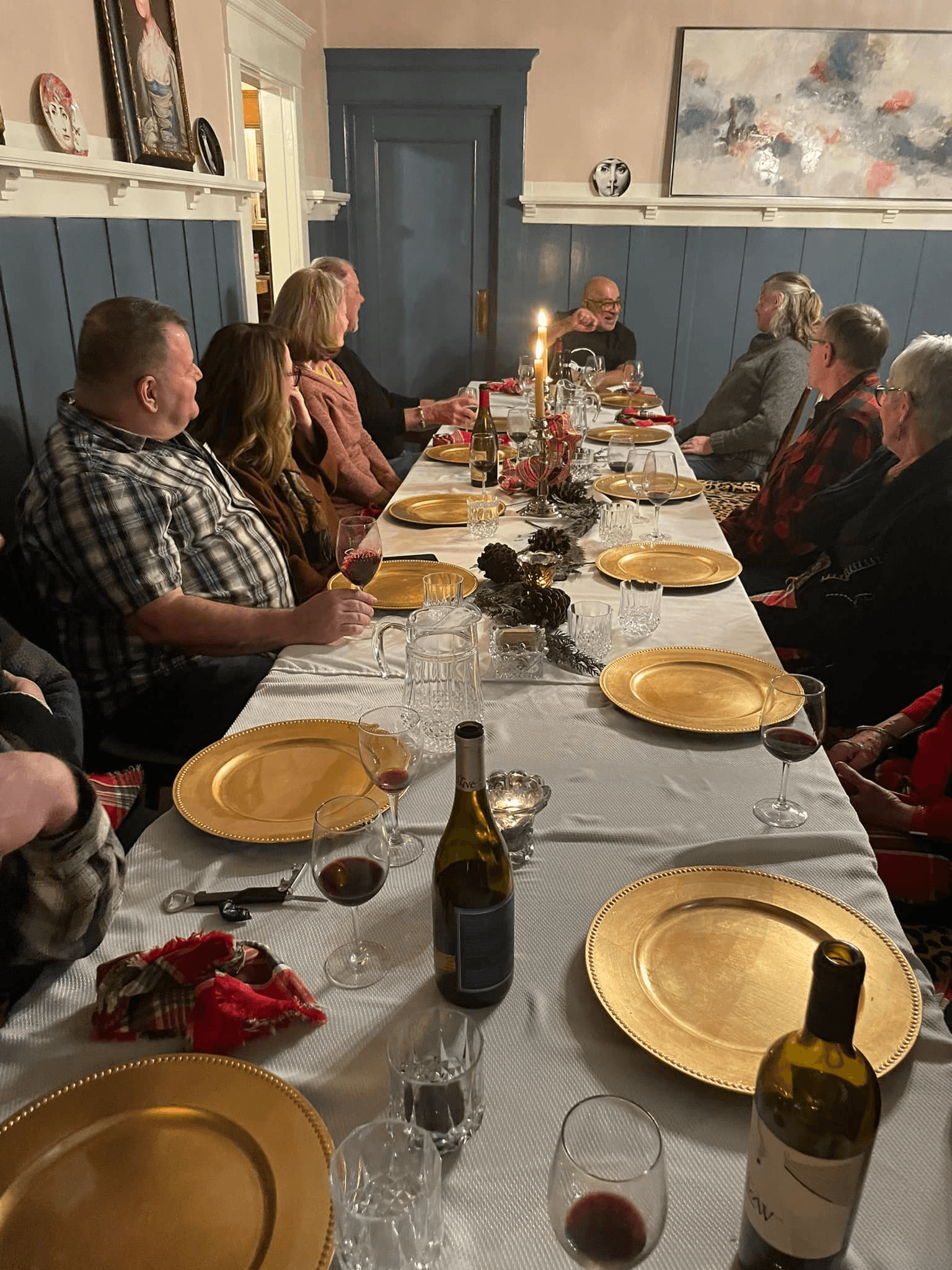 A festive dining table is set with gold plates and glasses, surrounded by a group of people enjoying an evening gathering.