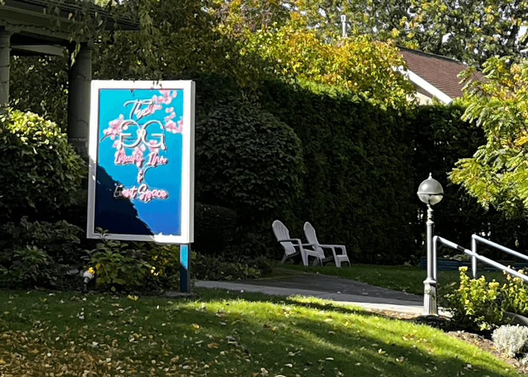 A colorful sign for a quaint inn and event space is set against a backdrop of greenery.