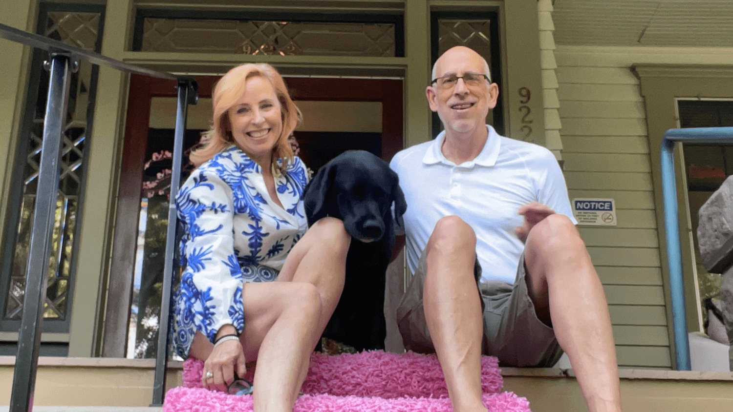 Karrie and Brian sitting on the front porch steps of The GG historic inn with their black dog between them