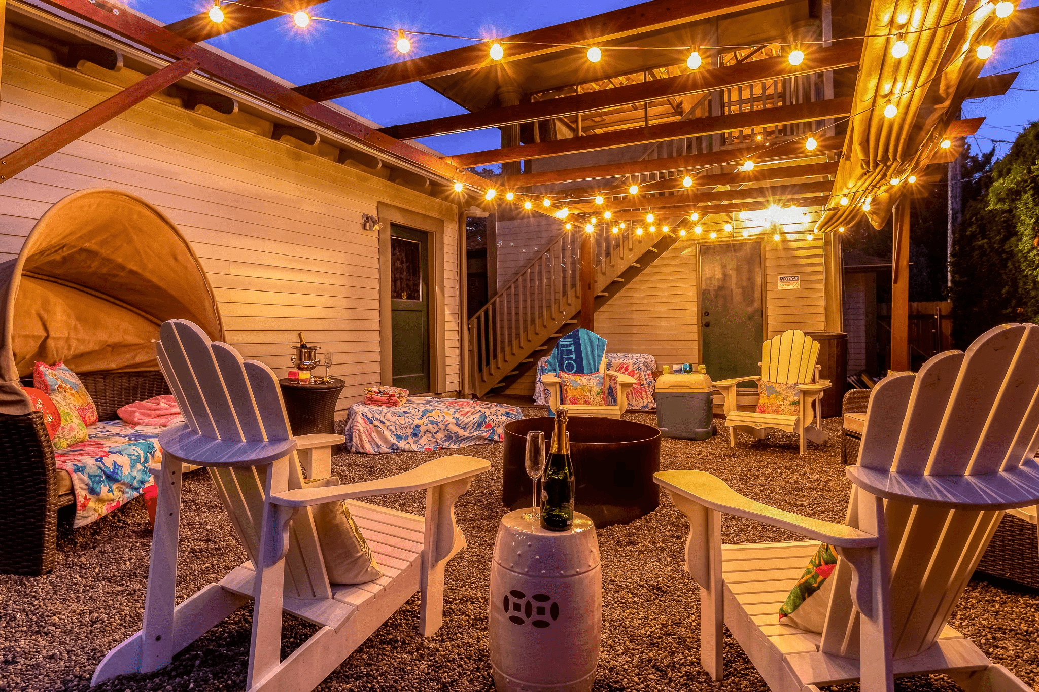 A cozy outdoor patio with string lights, adirondack chairs, and colorful blankets.