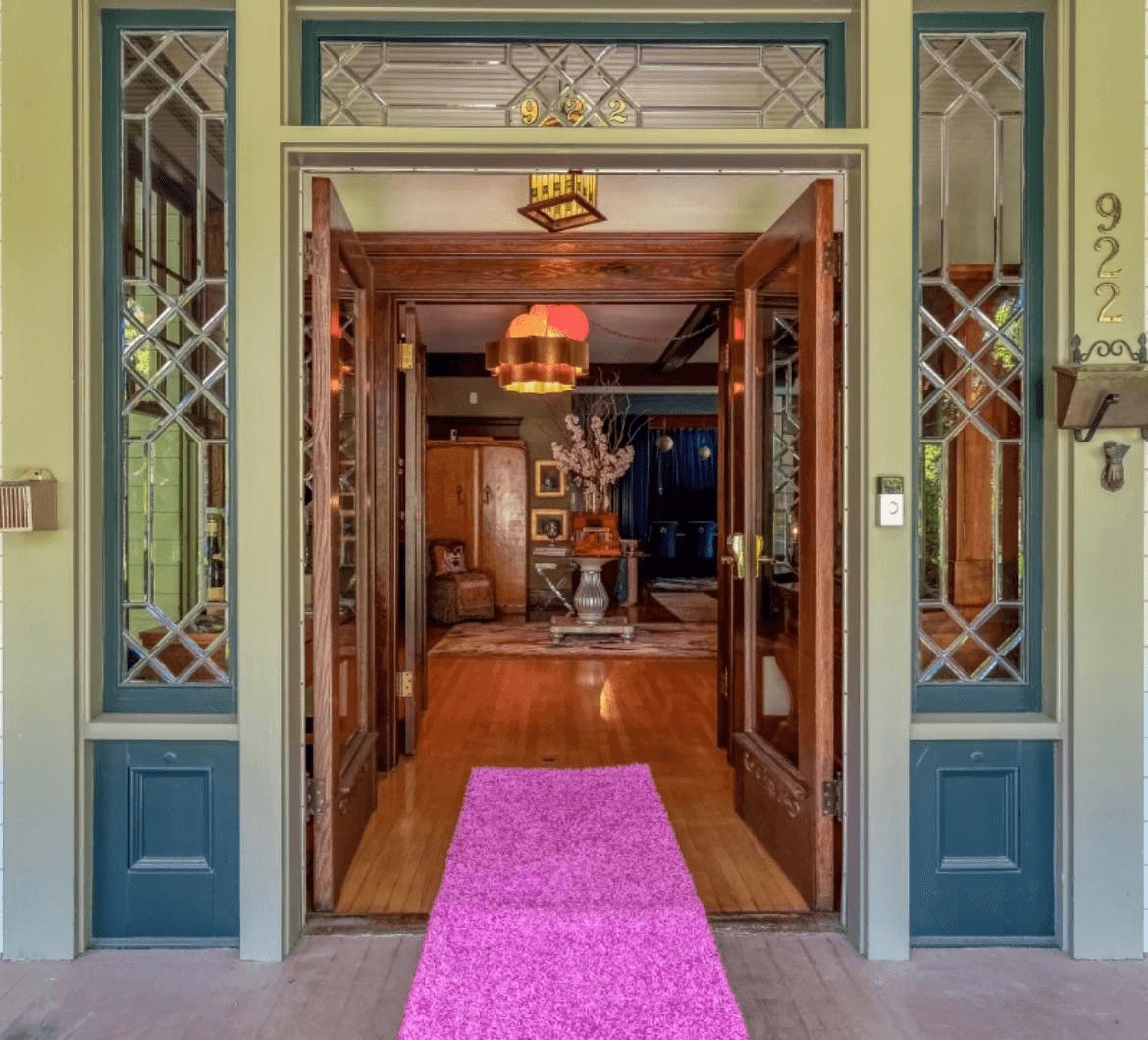 Hot pink carpet leads up porch steps to open door, looking inside entranceway